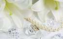 دو حلقه ازدواج کنار گردنبند مروارید و دانه های الماس و گلهای سفید