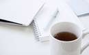 یک فنجان قهوه، دفترچه و خودکار روی میز