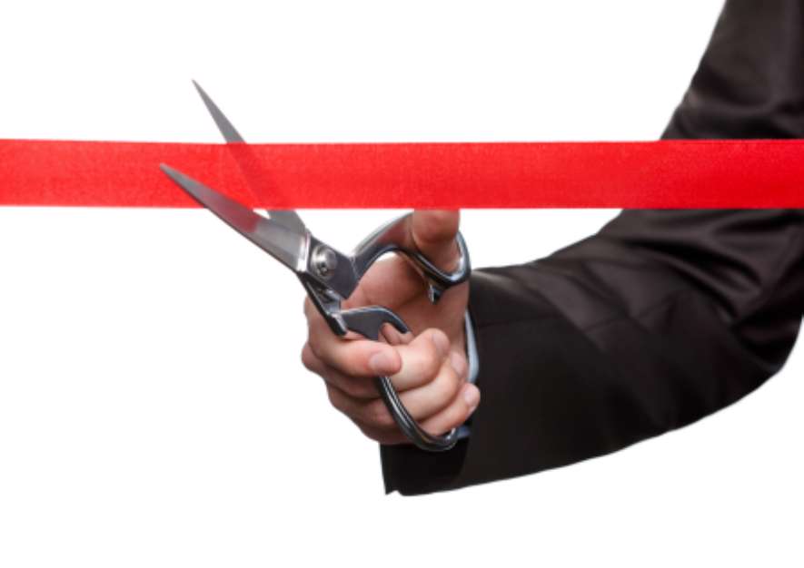 A man cutting a red satin ribbon with scissors
