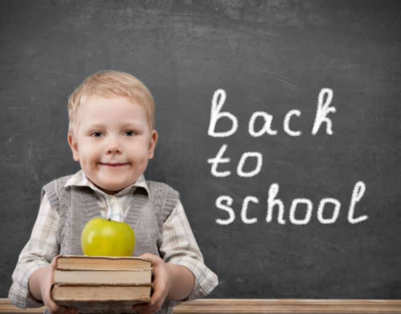 Cheerful smiling child with a book and apples stands at the blac