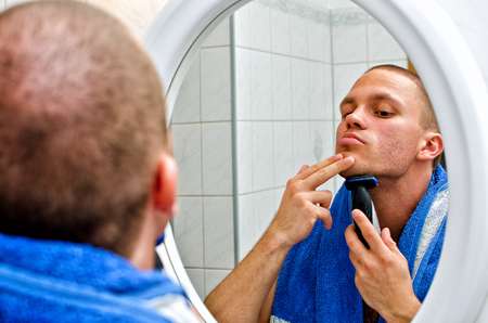 Male with towel shaving in bathroom in front of the mirror.