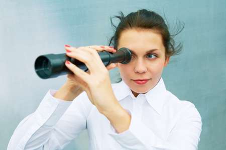 Young woman using telescope beside steel wall