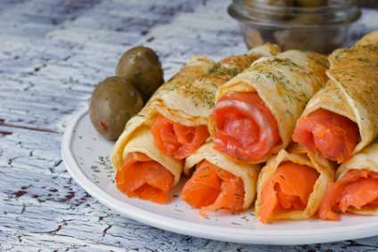 Rolls from pancakes with salmon on the white ceramic plate