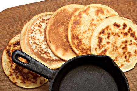 Four different round pancake and a small cast iron skillet lie on a wooden board