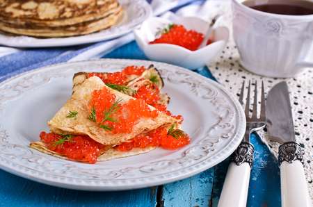 A stack of pancakes with red caviar on a background of old wooden surfaces