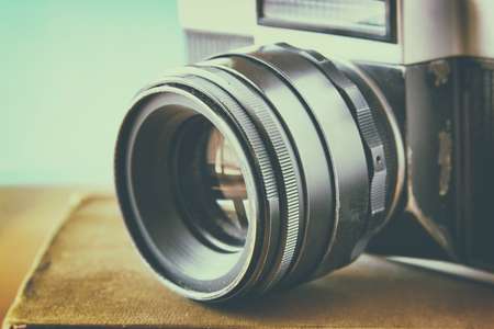 close up photo of old camera lens over wooden table. image is retro filtered. selective focus 
