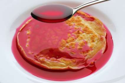 spoon with cherry syrup over pancakes on a white plate