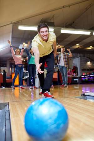 people, leisure, sport and entertainment concept - happy young man throwing ball in bowling club