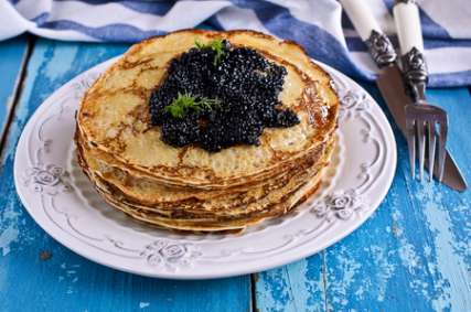 A stack of pancakes with black caviar on a background of old wooden surfaces