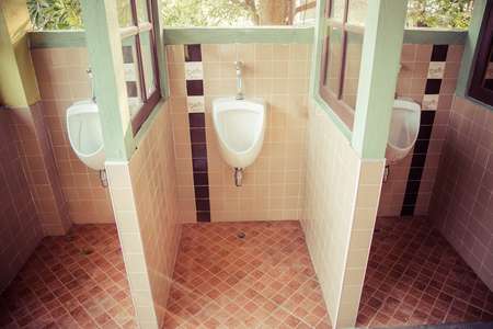 A row of urinals in tiled wall in a public restroom focusing, process color